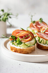 Three Bruschettas with baguette, bacon or meat, cream cheese, micro-greenery, fresh cucumber and sprouts, in composition on white plate on white textured background