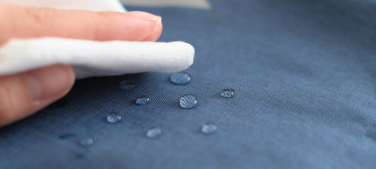 hand wipes drops of water from a cloth. Water drops on waterproof textile material. short depth of field. Waterproof fabric on sofa.