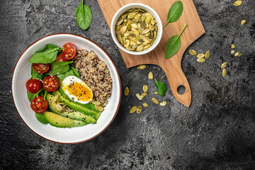 Keto diet plate quinoa, avocado, egg, tomatoes, spinach and sunflower seeds on dark background. Healthy food, ketogenic diet, diet lunch concept, place for text, top view