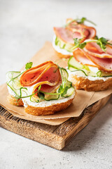 Bruschettas with baguette, bacon or meat, cream cheese, micro-greenery, fresh cucumber and sprouts,on wooden board on white textured background