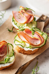 Bruschettas with baguette, bacon or meat, cream cheese, micro-greenery, fresh cucumber and sprouts, close-up in composition on wooden board on white textured background