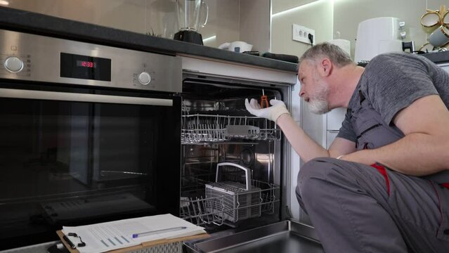 Man with toolbox repairing dishwasher in a household.