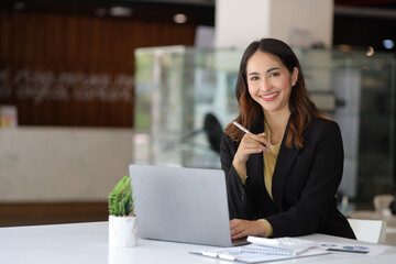 Portrait of a business woman working with a laptop on a desk in a spacious office. Looking at camera.