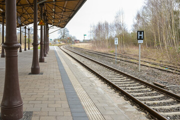 Fototapeta na wymiar Covered platform with vintage metal columns at the railroad tracks on the small country station in Schonberg, Mecklenburg, Germany, selected focus