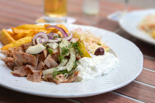Greek Gyros meal from roasted sliced meat with French fries, onions, coleslaw and tzatziki on a white plate in an outdoor restaurant, close-up shot, selected focus