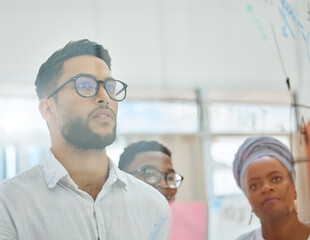 Obraz premium Focused on finding a winning strategy. Cropped shot of a group of diverse young businesspeople working on a glass wipe board in the boardroom.