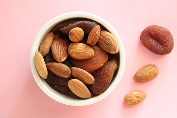 mix of almonds and apricots in the bowl, top view, pink background, natural sweet dry fruits