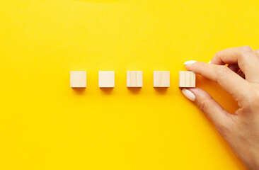 Business concept, hand places wooden cubes on yellow background