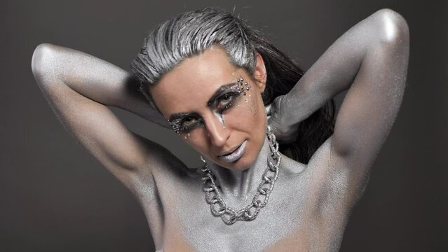 Beautiful woman with silver paint on her skin and hair plays with a chain in her hands.