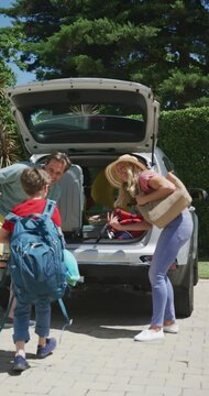 Vertical video of happy caucasian parents greeting son wearing rucksack at car