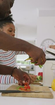 Vertical video of happy african american couple cooking at home