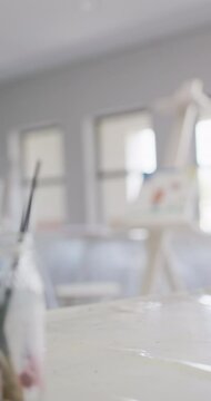 Vertical video of empty white painting classroom with painting equipment and easel