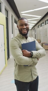 Vertical video of portrait of happy african american male teacher with documents