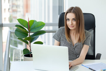 Beautiful business woman is using a laptop and smiling while working in office