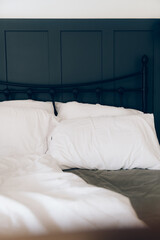 Empty undone king size bed in the morning with white duvet and pillows and grey sheet, morning routine. Modern minimalistic metal bed frame with panels on the wall