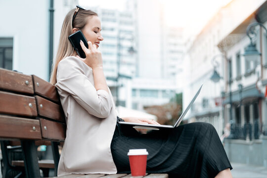 business woman with a laptop and a takeaway coffee talking on her smartphone .