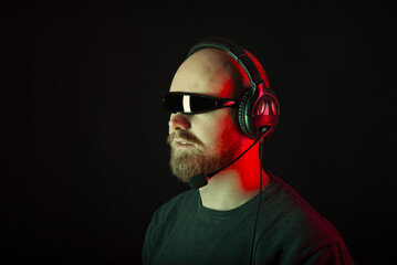 Serious bearded man wearing ciclop sunglasses is wearing headphones. Side view studio shot over black background. © Vulp