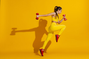 Fototapeta na wymiar Studio shot of sportive slim girl workout with sports equipment isolated on bright yellow studio background with shadow. Beauty, sport, action, fitness, youth concept.
