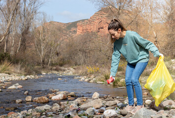 Young woman in a garbage collection picking up a can near the river