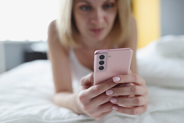 Woman lies in bed and looks at smartphone closeup