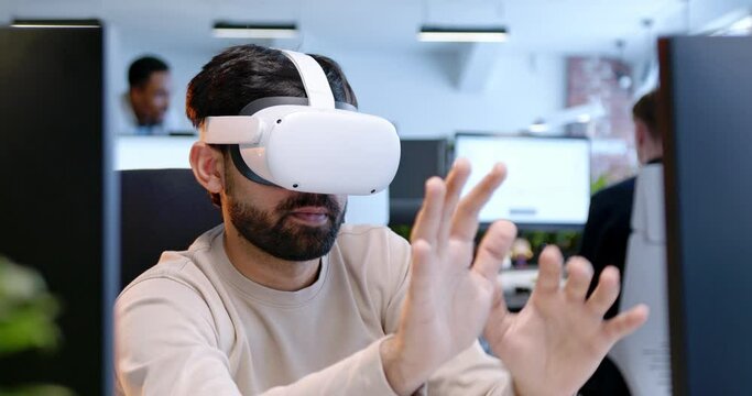 Close up of Arabian man in VR glasses sitting in office and moving hands in air. Male in headset tapping and scrolling in space. Virtual reality. Augmented gaming. Gamers. Coworking center.