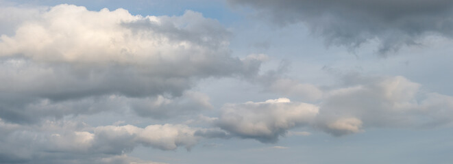 Fototapeta premium Panoramic view over soft blue sky with illuminated by sun rainy clouds as a background banner.