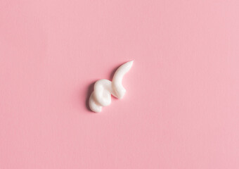 Smear of white face cream on pink background. Cosmetic product texture