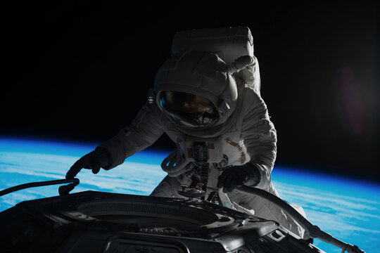 Female astronaut performing spacewalk, working on a outer part of a space craft