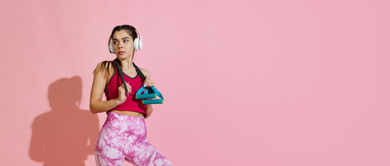 Flyer. Professional athlete, young girl training with sports equipment isolated on pink studio background with shadow. Beauty, sport, action, fitness, youth concept.