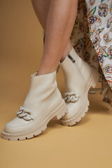 Fashionable woman with beige boots, leather shoes, studio shot. Casual lifestyle concept photo on a yellow pastel background.
