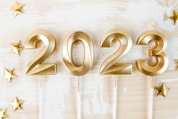 Numerals 2023 in gold color with sparkles in the form of stars on a white wooden table top view. Holiday New Year and Christmas.
