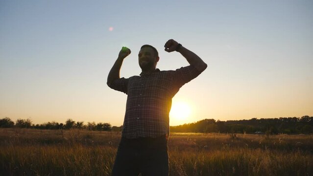 Happy guy outstretching arms up at summer meadow. Young man victoriously raising hands up on grass field at sunset. Male enjoying rest at beautiful nature. Concept of carefree and freedom. Dolly shot