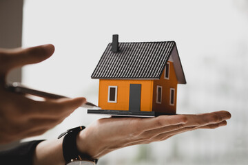 A real estate salesman holding a model of a small house to introduce customers, a sample house project where a salesperson advises customers. The concept of selling houses in the project.
