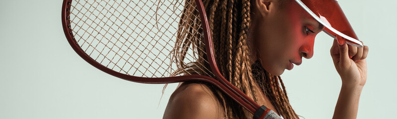 Sporty and beautiful. Side view of young african woman in sports clothes holding tennis racket on...