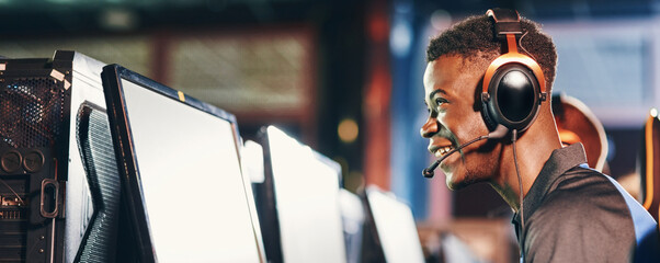 Side view of a happy excited african guy, professional gamer wearing headphones participating in...