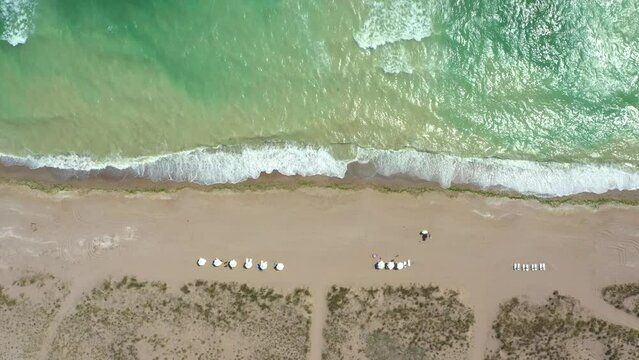 Aerial top down view of the beach without people on a hot sunny day. Sun umbrellas stand in yellow bright sand. Drone flying above the beach in Shabla, Bulgaria
