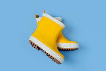 A pair of child yellow rain boots on blue background - obrazy, fototapety, plakaty
