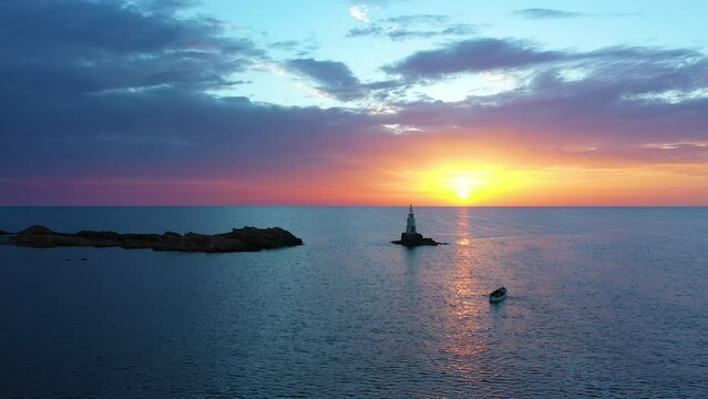 Flight over a sunny path to a lighthouse on an island and a beautiful sunrise. Fishing boat with fishermen to the lighthouse. Ahtopol, Bulgaria. 4K
