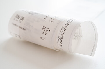 Rolled up shopping receipt, with some amounts visible, on a white surface. Inflation, rising prices...