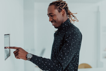 Smiling African American man using modern smart home system, controller on wall, positive young man...