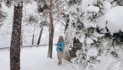 A woman stands and looks at nature with a thermocup in her hands next to a dome tent in glamping in the winter forest
