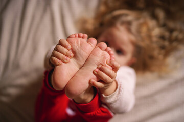 little girl holding her legs barefoot, baby feet close-up in focus