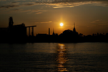Obraz premium Gorgeous scenic of Thai temple silhouettes and Industrial factory along Chao phraya river over sun at sunrise. Travel attraction in Thailand, Space for text, Focus and blur.