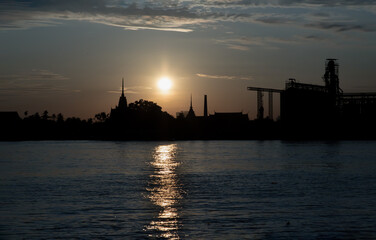 Gorgeous scenic of Thai temple silhouettes and Industrial factory along Chao phraya river over sun at sunrise. Travel attraction in Thailand, Space for text, Focus and blur.