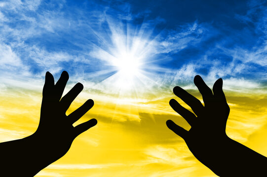 Silhouette of hands turned to the sky with a prayer for Ukraine