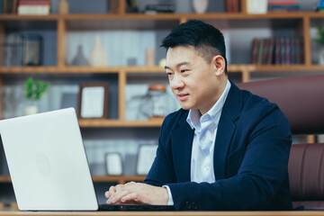 Concentrated businessman working on laptop in classic office, looking at monitor screen