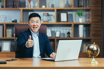 Portrait of a successful asian politician lawyer, man working at desk in classic office, looking at camera and smiling