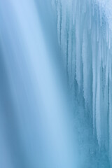 Winter landscape of a cascade captured with motion blur and framed by blue ice, Comstock Creek, Michigan, USA