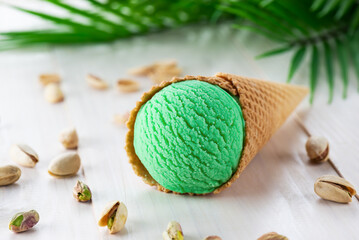 Fototapeta na wymiar Pistachio ice cream in a cone with a palm branch on a wooden table.