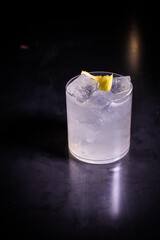 Vertical close-up of gin and tonic with lime and ice cubes in a glass on a bar table with lighting